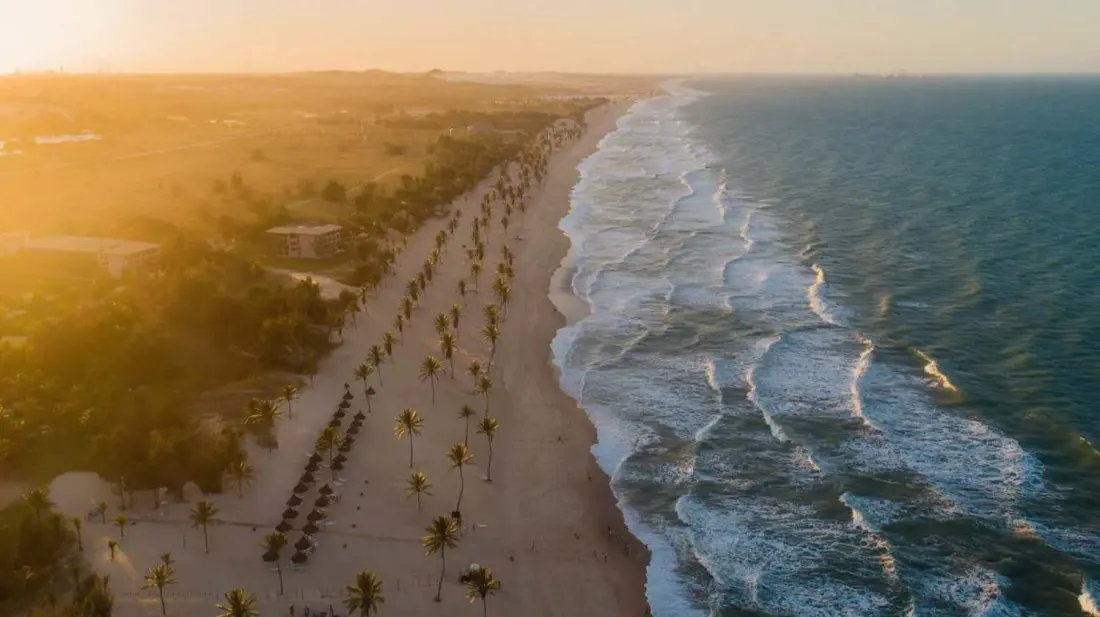 Vista aérea da Praia de Cumbuco com coqueiros e ondas ao pôr do sol
