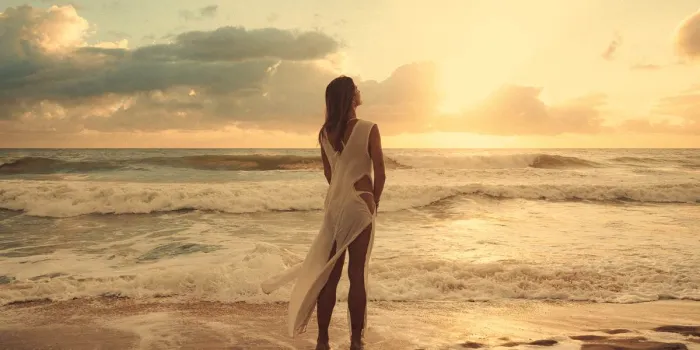 Mulher de vestido branco diante do pôr do sol na praia de Cumbuco